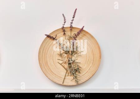 Dekoration für die Inneneinrichtung von Wohnzimmer, Esszimmer, Küche. Wandmontierte runde Holzplatte mit einem kleinen Blumenstrauß aus trockenen Lavendelzweigen, Rosmarin auf Stockfoto