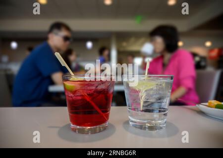 Ein Paar genießt einen Cocktail in der Flughafenlounge. Selektiver Fokus auf rote und klare Getränke im Vordergrund. Stockfoto