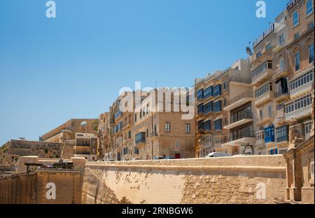 Detailaufnahme der Küste Maltas mit historischen Häusern hinter der dicken Mauer. Die typischen traditionellen Balkone sind an den Fassaden zu sehen. Stockfoto