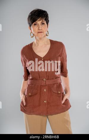 Herbstlicher Modetrend, brünette reife Frau in brauner Leinenjacke, die auf grau in die Kamera schaut Stockfoto