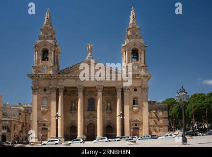 Vor der Pfarrkirche St. Publius' in Malta steht ein Mann und schaut auf die Kirche. Die Kirche aus dem 18. Jahrhundert besteht aus Kalkstein. Autos sind es Stockfoto