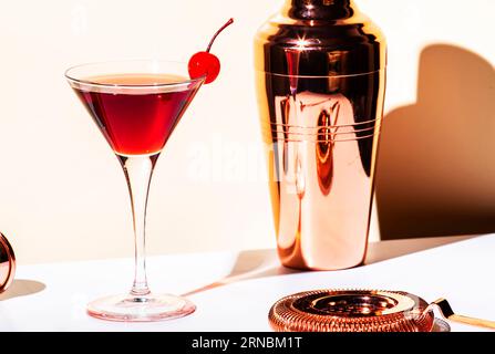 Schwarzer Manhattan alkoholischer Cocktail mit Whiskey und rotem Wermut, garniert mit Maraschino-Kirsche im Martiniglas. Beigefarbener Hintergrund, helles Licht Stockfoto