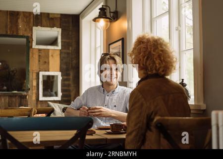 Glücklicher junger Mann, der mit einer Frau am Tisch in der Nähe des Fensters sitzt Stockfoto
