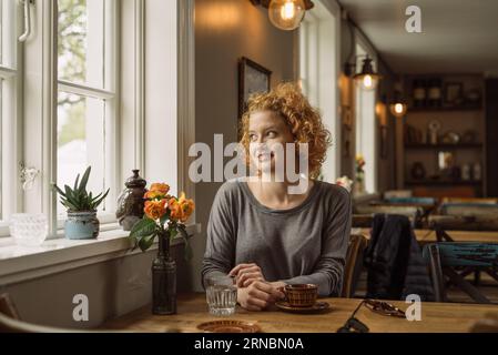 Glückliche junge Frau, die mit Kaffee am Tisch sitzt Stockfoto