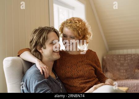 Fröhliches junges Paar, das sich zu Hause auf dem Stuhl umarmt Stockfoto