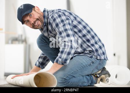 Männlicher Handwerker Rollteppich auf dem Boden zu Hause Stockfoto