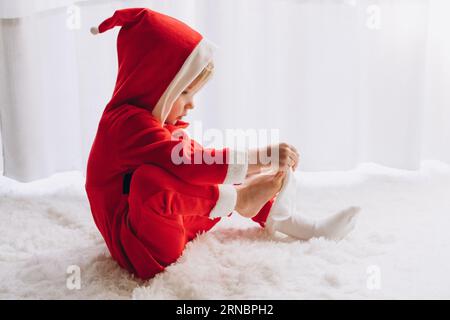 Das Kind sitzt im Weihnachtsmann und zieht Socken an Stockfoto