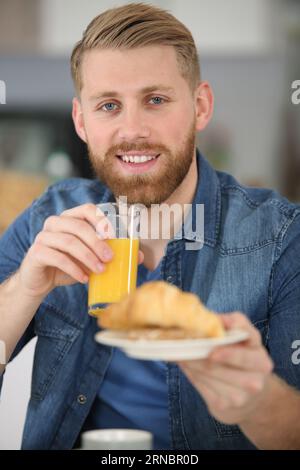 Mann, der ein Glas Saft hält und ein Croissant anbietet Stockfoto