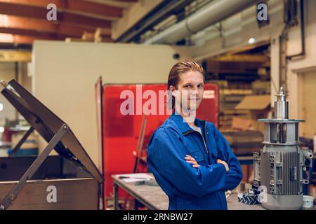 Glücklicher junger Mann, der bei Tageslicht in der Fabrik in der Nähe von Geräten steht Stockfoto