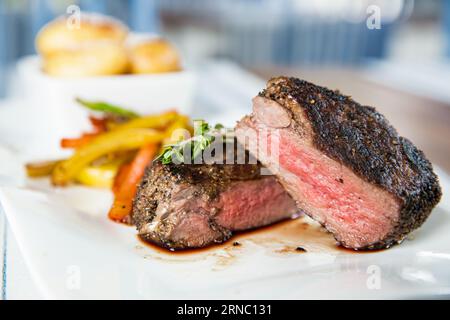 Appetitliches mittelseltenes, gegrilltes Rindersteak mit gebackenem Gemüse auf weißem Teller. Stockfoto
