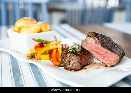 Appetitliches mittelseltenes, gegrilltes Rindersteak mit gebackenem Gemüse auf weißem Teller. Stockfoto