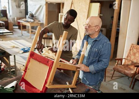 Porträt eines älteren Handwerkers mit Auszubildendem zur Reparatur alter Möbel in der Tischlerwerkstatt Stockfoto