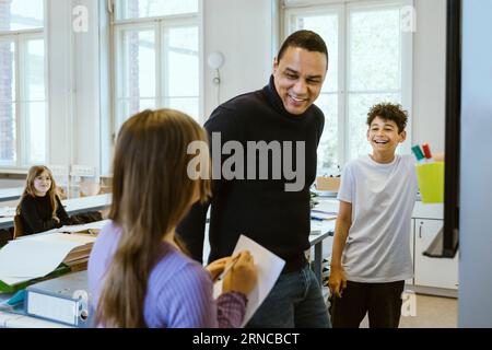 Glücklicher männlicher Lehrer, der Spaß mit den Schülern hat, während er im Klassenzimmer unterrichtet Stockfoto