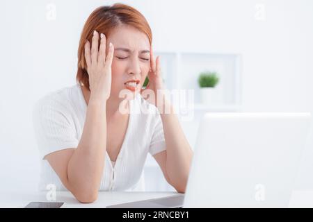 Müde asiatische Geschäftsfrau mit Kopfschmerzen im Büro Stockfoto