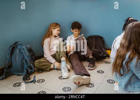 Junge und Mädchen lernen zusammen, während sie in der Nähe einer Mauer im Schulgebäude sitzen Stockfoto