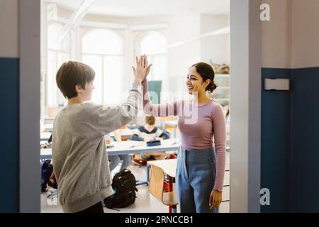 Lächelnde Lehrerin, die dem Schuljungen im Klassenzimmer High-Five gibt Stockfoto