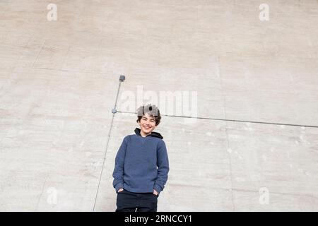 Blick auf den Happy Boy mit den Händen in Taschen, die im Recyclingzentrum an der Wand stehen Stockfoto