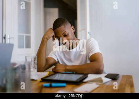 Müder junger Mann, der sich während des Studiums zu Hause auf den Ellbogen stützt Stockfoto