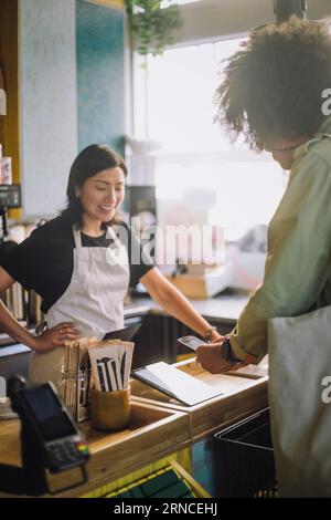 Lächelnde Verkäuferin, die beim Scannen an der Kasse in der Nähe eines männlichen Kunden mit mobiler Bezahlung steht Stockfoto
