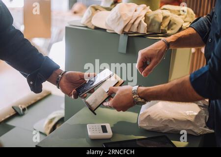 Freigestellte Hände eines männlichen Kunden und Angestellten, der an der Kasse im Bekleidungsgeschäft mobile Zahlungen tätigt Stockfoto