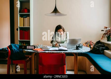 Junge Frau macht Hausaufgaben mit Laptop zu Hause Stockfoto