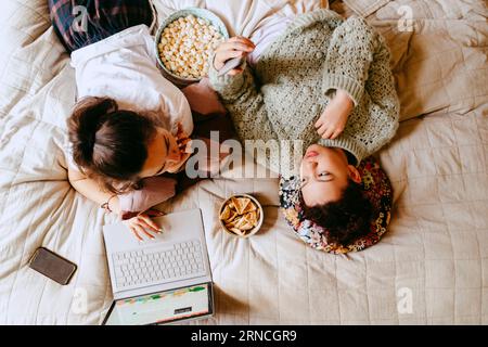 Direkt über der Aufnahme von Freundinnen, die sich unterhalten, während sie zu Hause auf dem Bett liegen Stockfoto