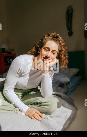 Porträt einer jungen Frau, die zu Hause mit der Hand auf dem Kinn sitzt Stockfoto