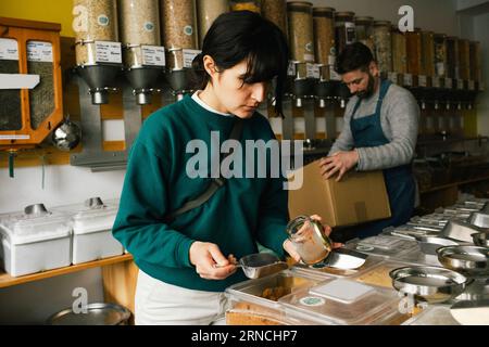 Frau, die beim Einkaufen in einem Bioladen den Becher mit Essen füllt Stockfoto