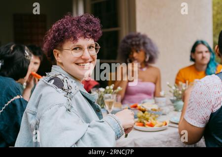 Seitenansicht Porträt einer glücklichen nicht-binären Person mit Freunden während der Party im Hinterhof Stockfoto