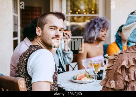 Porträt eines lächelnden schwulen Mannes mit Freunden am Esstisch während einer Dinnerparty im Hinterhof Stockfoto