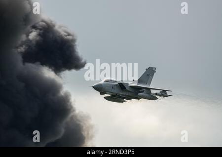 RAF Tornado Kampfjet fliegt mit hoher Geschwindigkeit an einer Wolke aus schwarzem Rauch während eines simulierten Bombenlaufs, Kampfszenario. Demonstration der Kriegsrolle Stockfoto