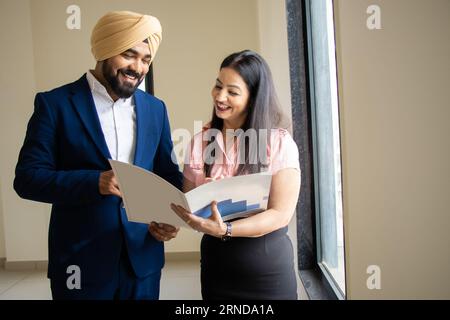 Indischer sikh-Geschäftsmann in formeller Kleidung diskutiert Arbeit mit junger weiblicher Sekretärin, die Akten im Firmenbüro hält. Stockfoto