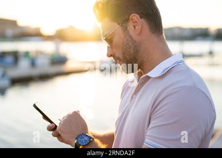 Ein lässiger, gutaussehender Mann, der in der Stadt telefoniert. Gut gekleideter Mann mit modischer Brille und Polo, der draußen telefoniert. Geschäftsmann Stockfoto