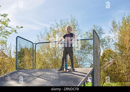 Boy on Scooter macht einen Trick und genießt seine Fahrt im Skatepark am bewölkten Frühlingstag. Junger Mann macht Trick auf dem Tretroller im Park. Fu Stockfoto