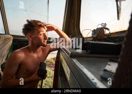 Ein reifer kaukasischer Mann in einem alten Zug, der mit einem nachdenklichen Ausdruck auf die Landschaft blickt Stockfoto