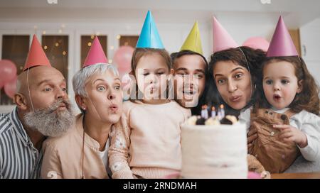 Alles Gute zum Geburtstag, zum Geschenk und zur großen Familie, die gemeinsam Kerzen mit Kuchen auf einer Party, einem Event und einer Feier bläst. Mutter, Vater und Großeltern begeistert Stockfoto