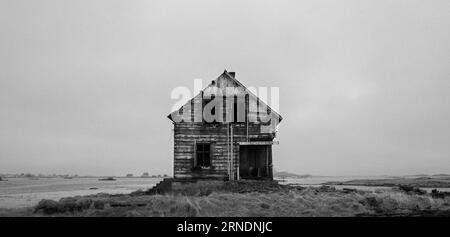Ein isoliertes verdorbenes Haus, isoliert auf der einsamen Prärie mit einem trockenen Grasland im Vordergrund Stockfoto