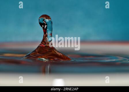 Wassertropfen treffen auf die Wasseroberfläche und bilden eine schöne Wassersäule. Wassertropfenabstraktion auf unscharfer blauer Oberfläche. Stockfoto