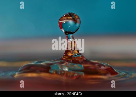 Wassertropfen treffen auf die Wasseroberfläche und bilden eine schöne Wassersäule. Wassertropfenabstraktion auf unscharfer blauer Oberfläche. Stockfoto