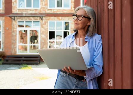 Eine gepflegte Frau mittleren Alters mit bob-Haarschnitt arbeitet frei mit einem Laptop auf der Straße Stockfoto