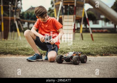 Junge mit elektrischem Autospielzeug mit Fernbedienung spielen draußen auf dem Bürgersteig und haben Spaß, während er seine Kindheit genießt Stockfoto