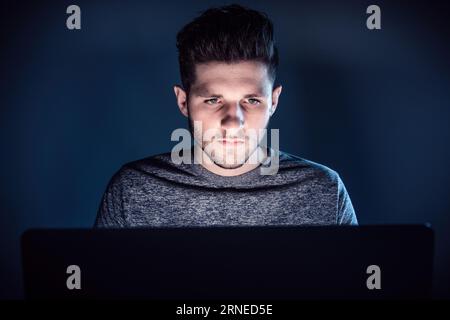 Der Mann in der Nacht vor dem Laptop schaut mit ernstem Gesicht auf den Bildschirm und erkennt, dass er Opfer von Betrug geworden ist Stockfoto