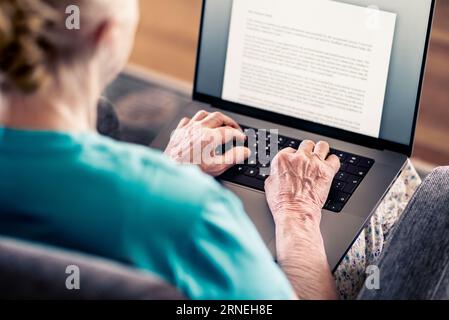 Alte Seniorin, die mit einem Laptop Text schreibt. Buch, Testament, Brief oder Tagebuch. Älterer Schriftsteller mit Notebook-pc. Eine reife Dame, die von zu Hause aus arbeitet. Stockfoto