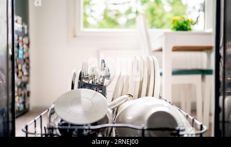 Geschirrspülmaschine. In einem offenen Geschirrspüler, Blick auf die Küche. Reinigen Sie Teller, Utensilien, Besteck und Topf im Waschtischgestell und Regal. Korb mit Gabel. Stockfoto