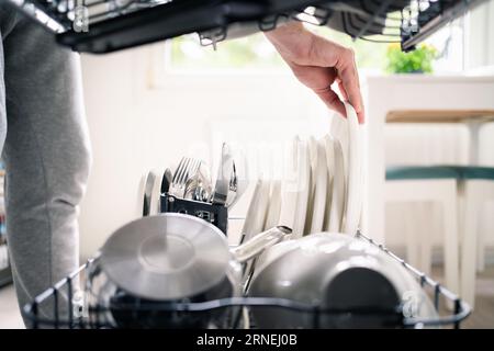 Geschirrspülmaschine. Waschmaschine in der Küche. Mann, der Geschirrspüler benutzt und Teller und Besteck entlädt, reinigt. Familienarbeit. Haushaltsarbeiten. Stockfoto