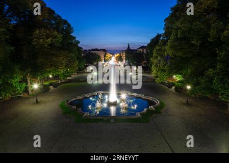 Beleuchteter Brunnen mit Wasserstrahlen vor der Luitpold-Brücke und der Prinzregenten-Straße bei blauer Stunde in der Abenddämmerung in München, Bayern, Deutschland Stockfoto