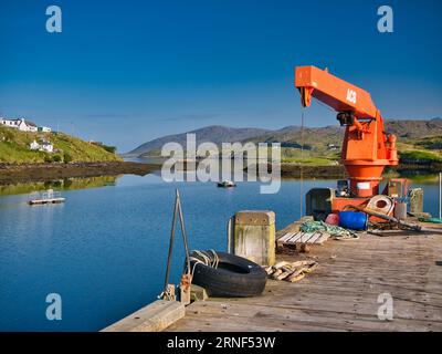 An einem klaren Sommermorgen, der Anlegestelle am Nordhafen der Insel Scalpay in den Äußeren Hebriden, Schottland, Großbritannien. Ein orangefarbener ACB-Kran wird angezeigt Stockfoto