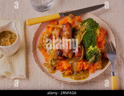 Cumberland-Würstchen mit pürierten Süßkartoffeln und Zwiebelsoße. Stockfoto