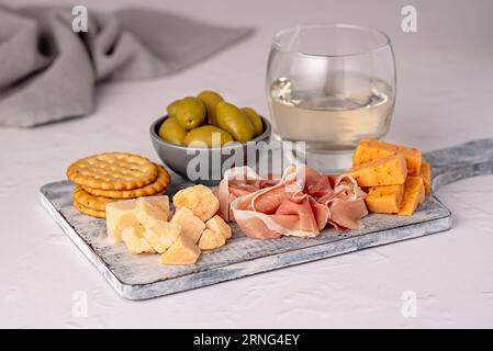 Lebensmittelfotografie von Antipasto, Weißwein, Käse, Schinken, serrano, Oliven, Prosciutto, Cracker, Parmesan, Cheddar, Delikatessen Stockfoto