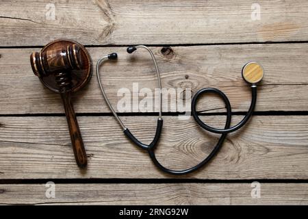 Stethoskop und Hammer des Richters liegen auf einem hölzernen Hintergrund, medizinisches Gericht, Recht und Gerechtigkeit Stockfoto